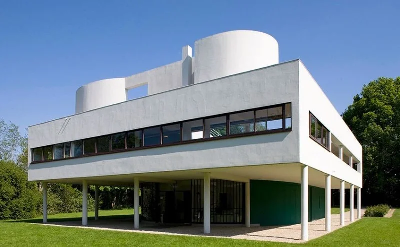 Villa Savoye vista frontal: pilotis brancos no terreo, faixa horizontal de janela no segundo pavimento e cilindro do terraco-jardim emergindo no topo