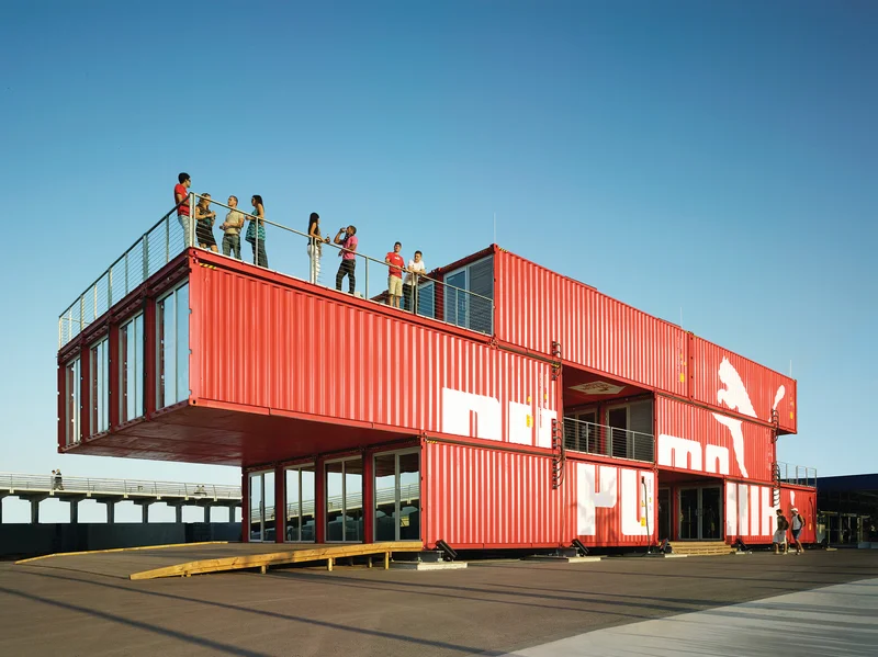 Loja em containers vermelhos empilhados com balanço estrutural — exemplo do potencial portante do COR-TEN