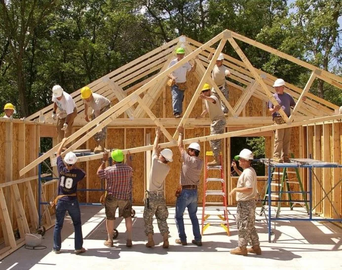 Mulher trabalhando na construção de uma parede de adobe, moldando o barro com as mãos.