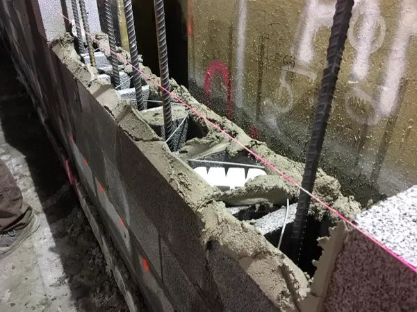 Parede de blocos de concreto com vergalhões e argamassa durante a construção
