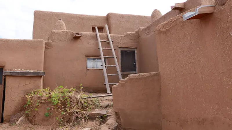 Construção em adobe no estilo dos pueblos do sudoeste dos EUA — paredes de terra crua e escada de madeira tradicional