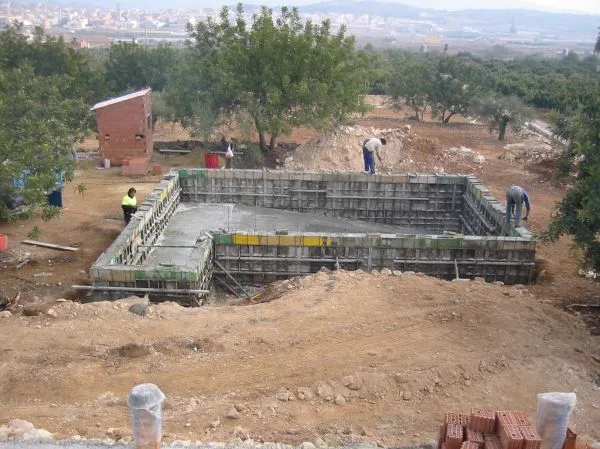 Fôrma de madeira e concreto de uma piscina sendo construída em terreno com operários
