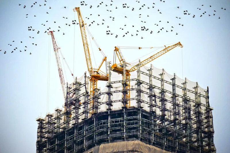Canteiro de obras real com estrutura de concreto em construção, gruas amarelas e armação de pilares aparente, ilustrando fluxo de cargas do cálculo estrutural
