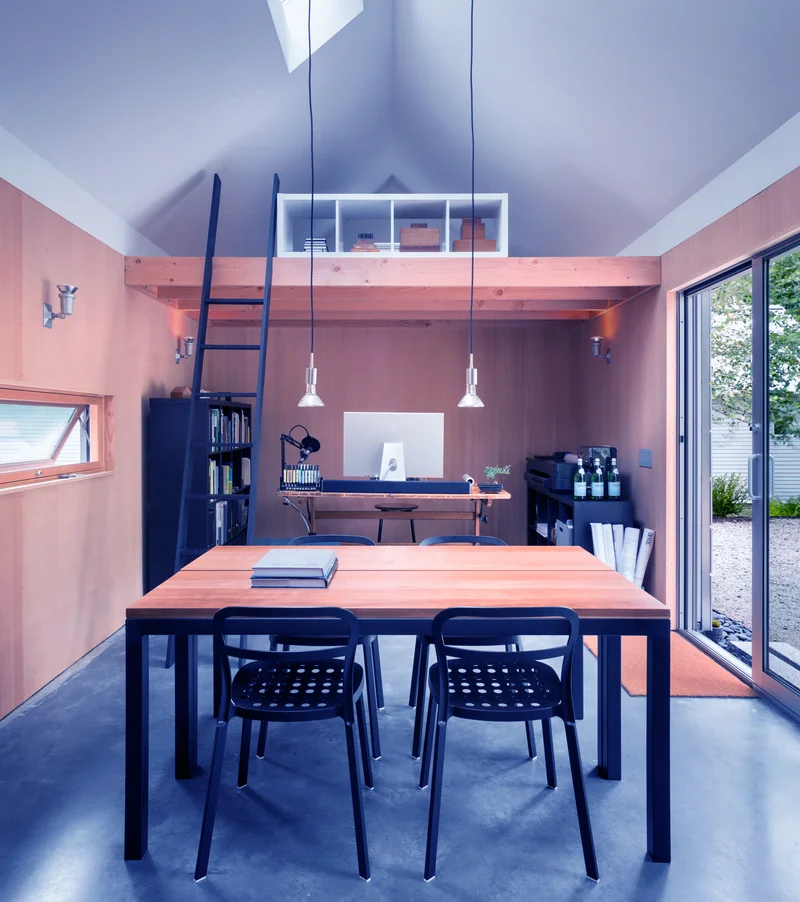 Pequeno escritório de arquitetura com mesa de trabalho compartilhada, estante de livros e ateliê — espaço típico de quem está empreendendo na arquitetura