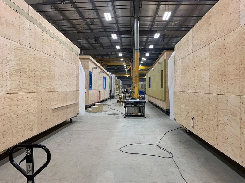 Operários montando um módulo de uma casa pré-fabricada em um canteiro de obras.