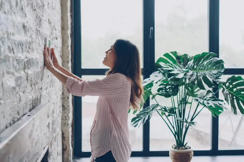 Moradora acionando painel de automação predial em residência sustentável — controle inteligente de iluminação e climatização