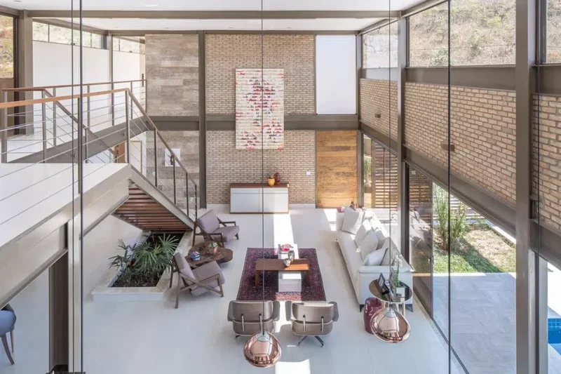 Ambiente com pé-direito duplo, mezanino e fechamento em vidro: a altura entrega volume porque vem acompanhada de iluminação natural abundante