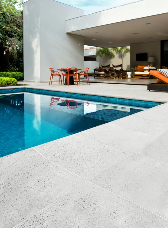 Piscina de fibra em formato de rim, com um deck de piso cimentício atérmico e um belo paisagismo com palmeiras.