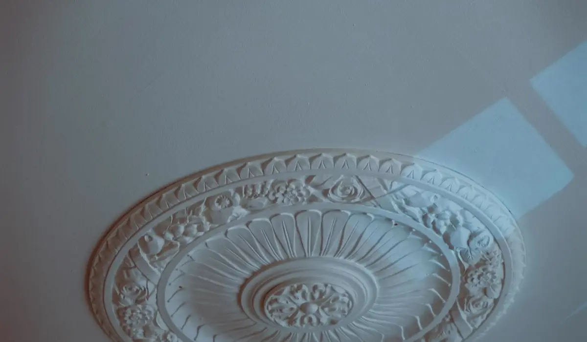 Roseta decorativa de gesso staff em teto branco, com detalhes florais em alto-relevo, peca pre-fabricada instalada
