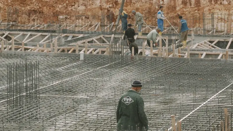Equipe concretando laje armada com malha de barras em canteiro de obras com solo de fundacao ao fundo